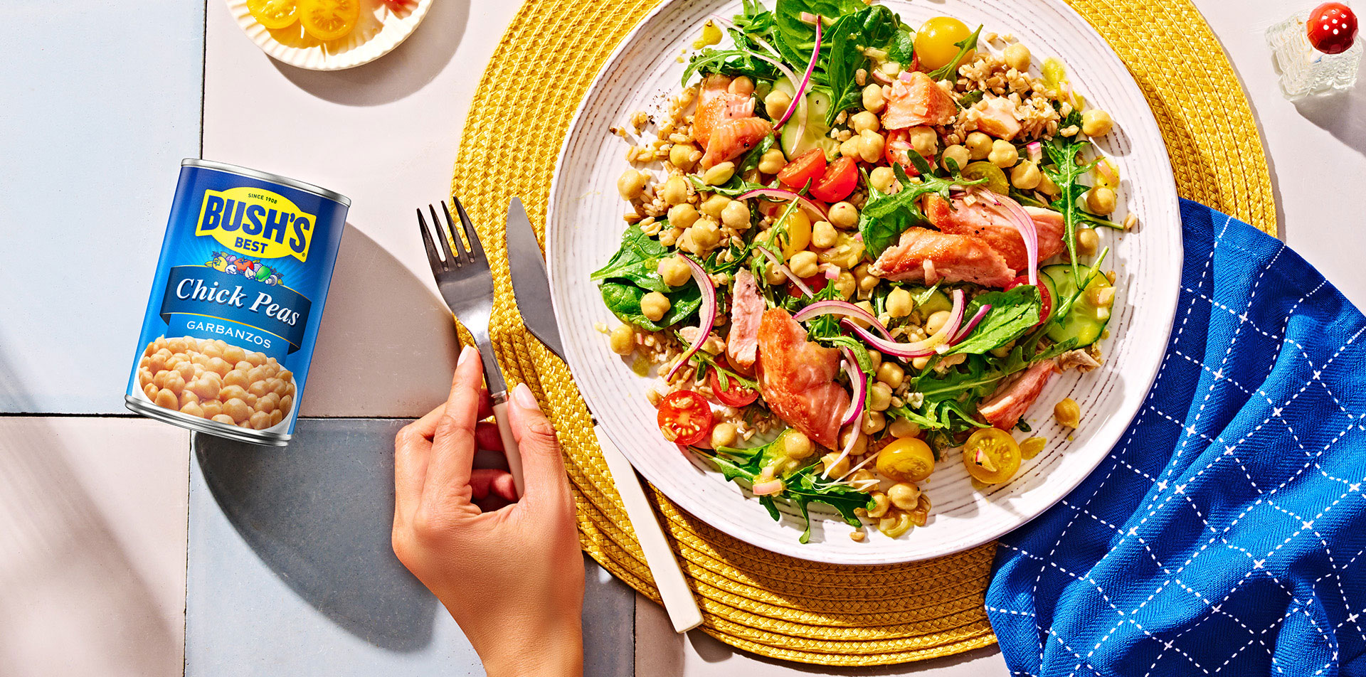 Mediterranean Farro & Salmon Salad on a white plate with a yellow placemat and a blue napkin.