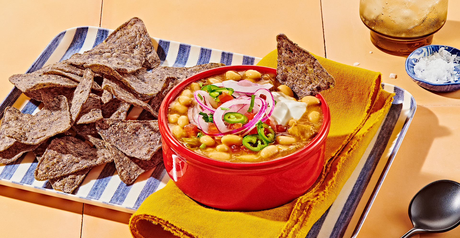 Chicken chili with white beans and jalapenos in a red bowl with blue corn tortilla chips