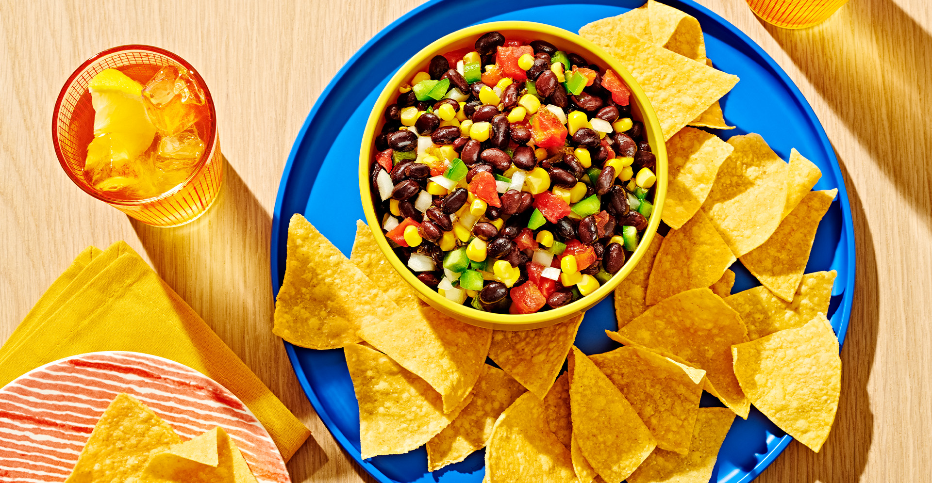 Black bean salsa and tortilla chips on a blue plate with a glass of ice water